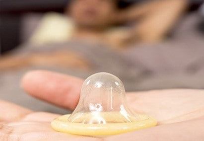Ein geöffneter, nicht ausgerollter transparenter Kondom liegend auf einer Hand.